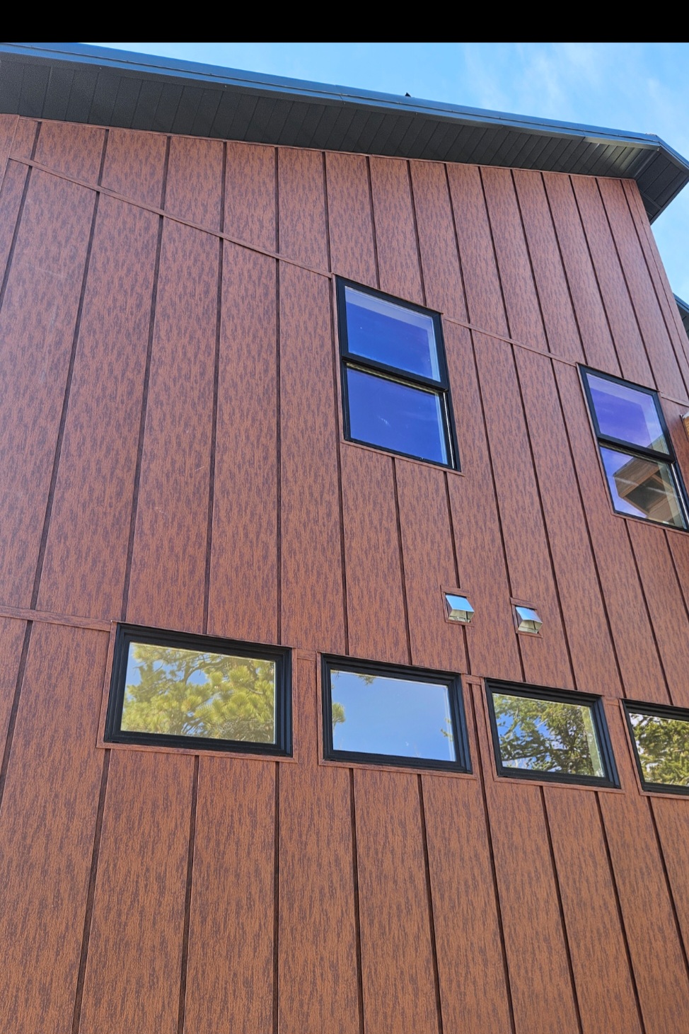 Rust-tone vertical panel metal siding installed on a Woodland Park home by Rawson Roofing